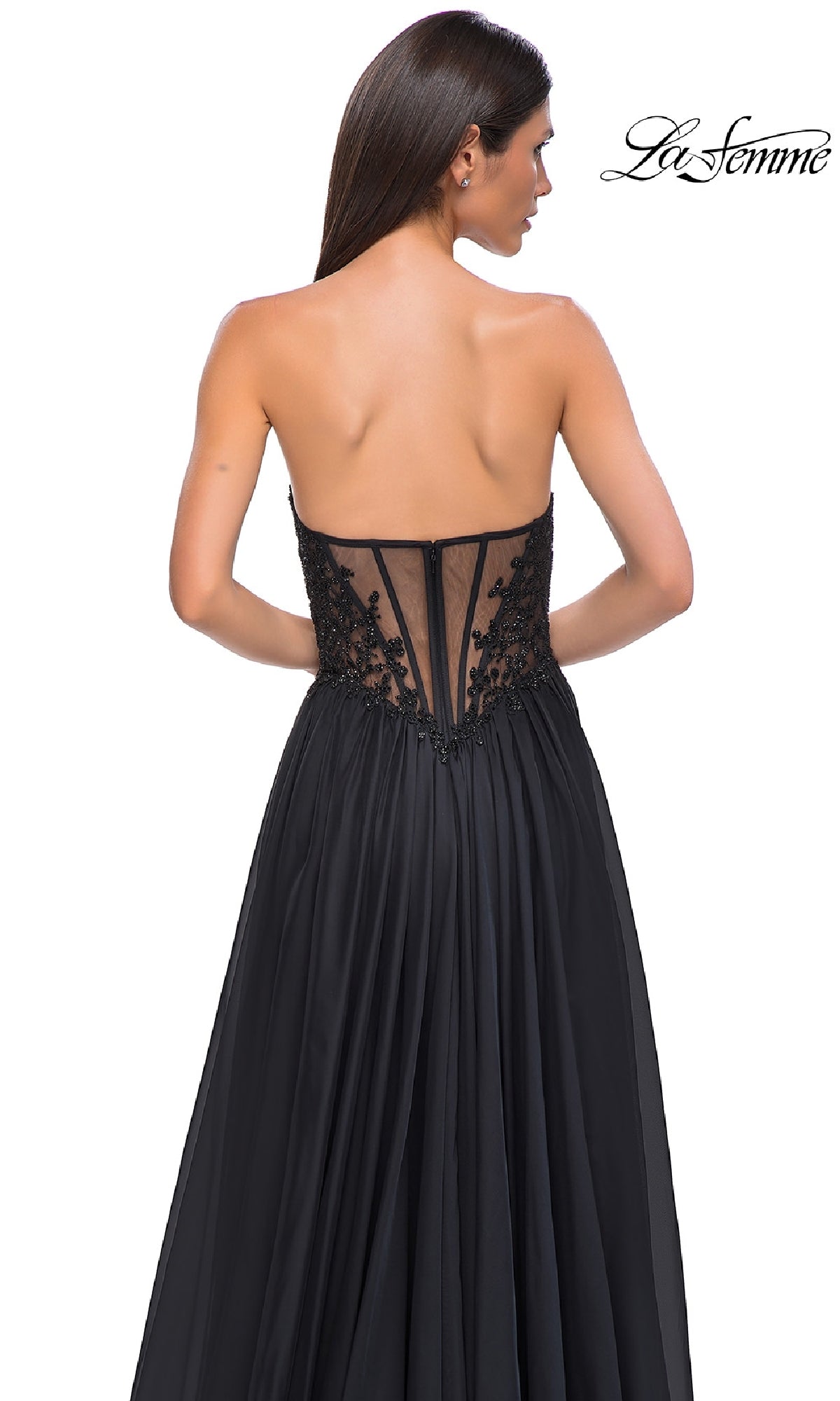 A woman models the La Femme 32804, a strapless long A-line prom dress featuring a sheer, beaded lace bodice and a flowing skirt, shown from the back.